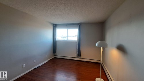 This space features hardwood floors, light gray walls, and a window with dark curtains - 12 11265 31 Avenue, Edmonton, AB - Indoor Photo Showing Other Room