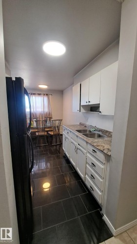 Kitchen featuring black tiled flooring, white cabinetry, a double basin sink, and a black refrigerator - 12 11265 31 Avenue, Edmonton, AB - Indoor