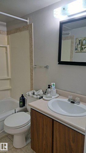 This bathroom features a vanity with a wood-toned cabinet and a light-colored countertop, a white sink, and a framed mirror - 12 11265 31 Avenue, Edmonton, AB - Indoor Photo Showing Bathroom