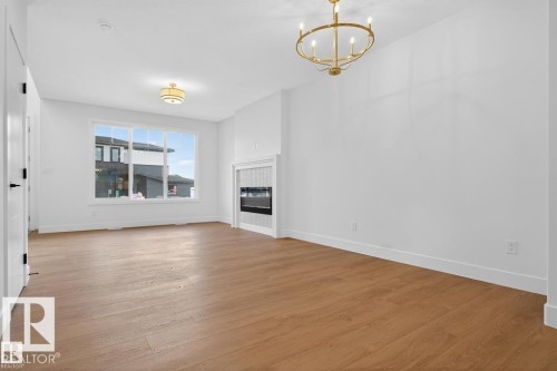 Unfurnished living room with hanging lights, light wood-style flooring, and a glass covered fireplace - 45 Rosa Crescent, St. Albert, AB - Indoor Photo Showing Other Room With Fireplace