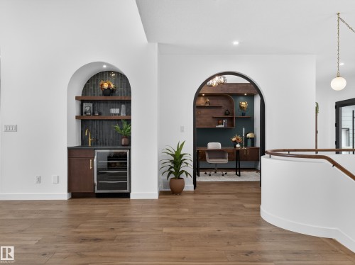 Indoor wet bar featuring arched walkways, wine cooler, wood finished floors, open shelves, and built in shelves - 7104 54 Avenue, Beaumont, AB - Indoor Photo Showing Other Room