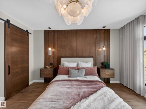 Bedroom featuring a barn door, wood walls, wood finished floors, access to exterior, and an accent wall - 7104 54 Avenue, Beaumont, AB - Indoor Photo Showing Bedroom