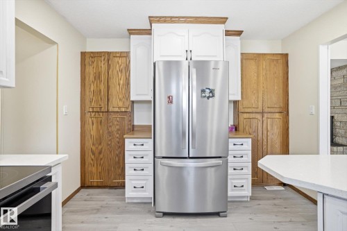 Two tone kitchen featuring freestanding refrigerator, light wood-type flooring, black range with electric cooktop, two tone cabinetry, and light stone counters - 83 Bellevue Crescent, St. Albert, AB - Indoor Photo Showing Kitchen