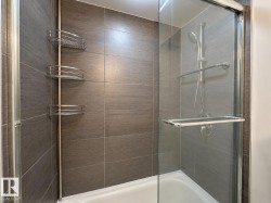 Walk-in shower featuring gray subway tile surround, clear glass enclosure, a handheld showerhead, and built-in shelving - 