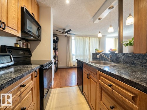 Kitchen with black appliances, dark countertops, wood finish cabinets, hanging light fixtures, and a textured ceiling - 1401 10883 Saskatchewan Drive, Edmonton, AB - Indoor Photo Showing Kitchen