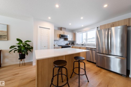 Kitchen featuring stainless steel appliances, a center island, a breakfast bar area, light wood-style flooring, and light wood finish cabinets - 112 Stonehouse Way, Leduc, AB - Indoor Photo Showing Kitchen With Upgraded Kitchen