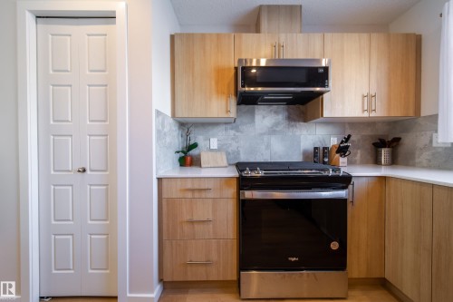 Kitchen featuring stainless steel appliances, modern cabinets, light stone counters, light wood finish cabinets, and tasteful backsplash - 112 Stonehouse Way, Leduc, AB - Indoor Photo Showing Kitchen