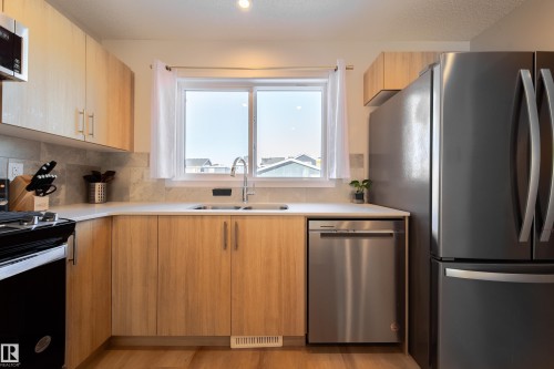 Kitchen featuring stainless steel appliances, light wood finish cabinets, light wood-style floors, and decorative backsplash - 112 Stonehouse Way, Leduc, AB - Indoor Photo Showing Kitchen With Double Sink
