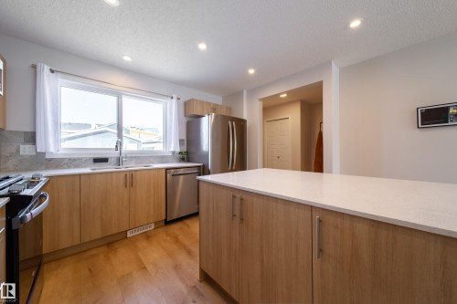 Kitchen with light stone countertops, light wood-style floors, recessed lighting, stainless steel appliances, and modern cabinets - 112 Stonehouse Way, Leduc, AB - Indoor Photo Showing Kitchen