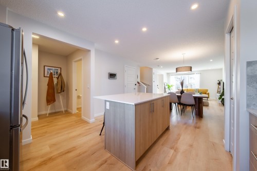 Kitchen with freestanding refrigerator, a kitchen island, light wood-type flooring, pendant lighting, and a kitchen bar - 112 Stonehouse Way, Leduc, AB - Indoor Photo Showing Kitchen