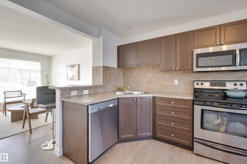 Kitchen with stainless steel appliances, a textured ceiling, light countertops, a peninsula, and light wood-type flooring - 21 6032 38 Avenue, Edmonton, AB - Indoor Photo Showing Kitchen