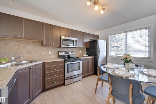 Kitchen with stainless steel appliances, light countertops, light wood-style flooring, dark wood finish cabinets, and a textured ceiling - 21 6032 38 Avenue, Edmonton, AB - Indoor Photo Showing Kitchen With Double Sink