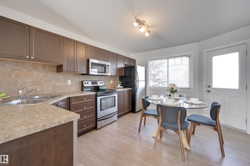 Kitchen featuring stainless steel appliances, light countertops, dark wood finish cabinets, light wood-type flooring, and a textured ceiling - 21 6032 38 Avenue, Edmonton, AB - Indoor Photo Showing Kitchen With Double Sink