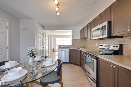 Kitchen with stainless steel appliances, light countertops, light wood-type flooring, a textured ceiling, and dark wood finish cabinets - 21 6032 38 Avenue, Edmonton, AB - Indoor