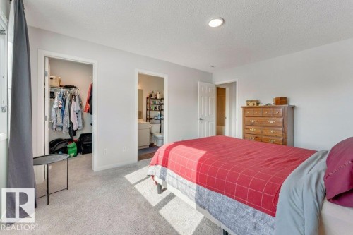 Bedroom featuring a spacious closet, light colored carpet, a textured ceiling, and connected bathroom - 1323 South Creek Link, Stony Plain, AB - Indoor Photo Showing Bedroom