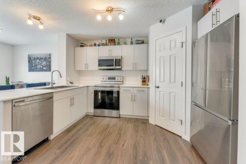 Kitchen with stainless steel appliances, light wood-type flooring, a peninsula, a textured ceiling, and white cabinets - 1323 South Creek Link, Stony Plain, AB - Indoor Photo Showing Kitchen With Stainless Steel Kitchen
