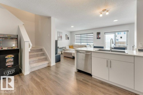 Kitchen featuring open floor plan, light wood-style flooring, stainless steel dishwasher, a peninsula, and a textured ceiling - 1323 South Creek Link, Stony Plain, AB - Indoor Photo Showing Kitchen