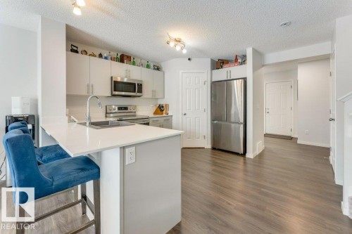 Kitchen featuring stainless steel appliances, a peninsula, a breakfast bar area, light countertops, and dark wood-style floors - 1323 South Creek Link, Stony Plain, AB - Indoor Photo Showing Kitchen With Stainless Steel Kitchen With Double Sink