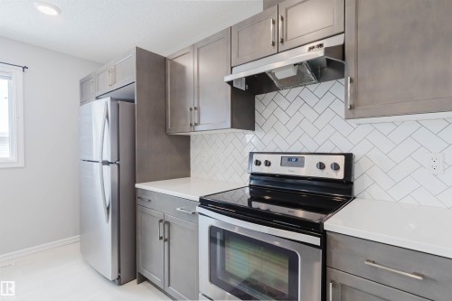 The kitchen features grey cabinetry, white countertops, a white herringbone tile backsplash, and stainless steel appliances including a refrigerator and range - 326 Desrochers Boulevard, Edmonton, AB - Indoor Photo Showing Kitchen With Stainless Steel Kitchen