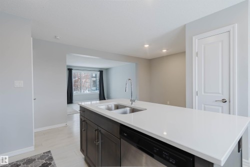 The kitchen features a large island with a double sink and a modern faucet, complemented by dark wood cabinetry and a dishwasher - 326 Desrochers Boulevard, Edmonton, AB - Indoor Photo Showing Kitchen With Double Sink