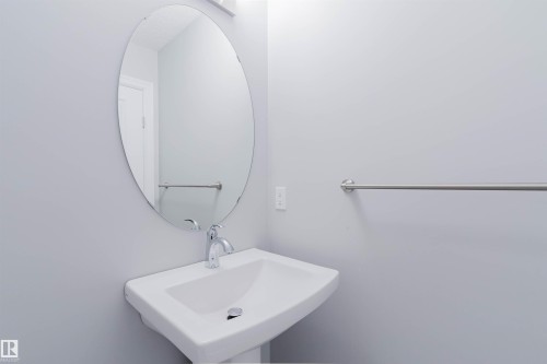 A bathroom featuring a white pedestal sink with a chrome faucet, an oval mirror, and a towel bar - 326 Desrochers Boulevard, Edmonton, AB - Indoor Photo Showing Bathroom