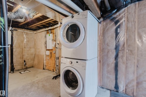 The property includes a laundry area with a stacked washer and dryer unit, exposed ceiling joists, and insulated walls - 326 Desrochers Boulevard, Edmonton, AB - Indoor Photo Showing Laundry Room
