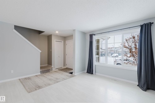 The property features light-colored flooring, a staircase with a carpeted tread, and a large window with privacy curtains - 326 Desrochers Boulevard, Edmonton, AB - Indoor Photo Showing Other Room
