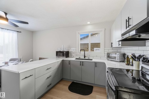 Kitchen with black range with electric cooktop, a peninsula, gray cabinets, light wood-style floors, and backsplash - 4615 49 Avenue, Redwater, AB - Indoor Photo Showing Kitchen