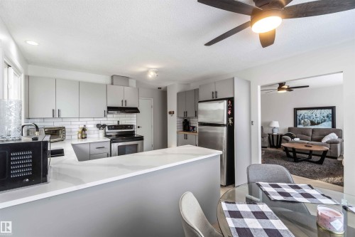 Kitchen featuring gray cabinets, stainless steel appliances, decorative backsplash, a peninsula, and a textured ceiling - 4615 49 Avenue, Redwater, AB - Indoor Photo Showing Kitchen