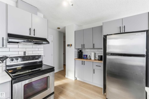 Kitchen with stainless steel appliances, butcher block countertops, exhaust hood, gray cabinetry, and light wood-type flooring - 4615 49 Avenue, Redwater, AB - Indoor Photo Showing Kitchen