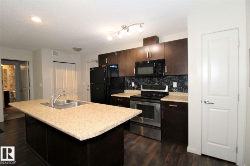 Kitchen with black appliances, dark wood-type flooring, light countertops, an island with sink, and dark wood finish cabinets - 430 5515 7 Avenue, Edmonton, AB - Indoor Photo Showing Kitchen With Double Sink