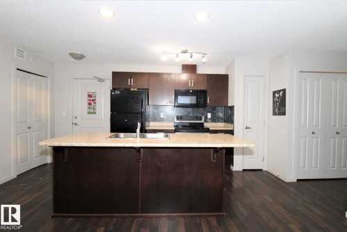 Kitchen with dark wood finish cabinets, black appliances, a center island with sink, dark wood finished floors, and a textured ceiling - 430 5515 7 Avenue, Edmonton, AB - Indoor Photo Showing Kitchen With Double Sink