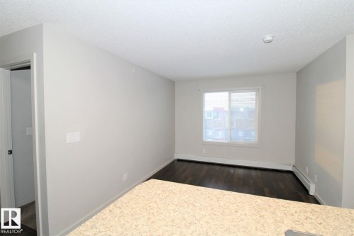 Unfurnished room featuring dark wood-style flooring, baseboard heating, a baseboard radiator, and a textured ceiling - 430 5515 7 Avenue, Edmonton, AB - Indoor Photo Showing Other Room