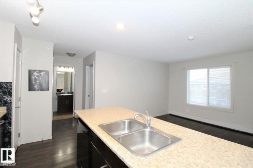 Kitchen featuring dark wood finished floors, light countertops, dishwasher, dark cabinetry, and a textured ceiling - 430 5515 7 Avenue, Edmonton, AB - Indoor Photo Showing Kitchen With Double Sink