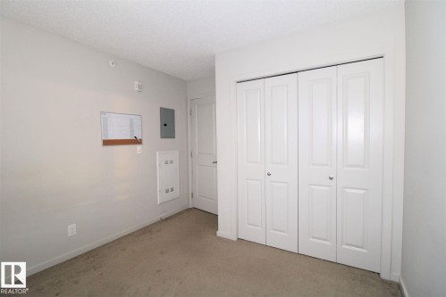 Unfurnished bedroom featuring light carpet, a closet, a textured ceiling, and electric panel - 430 5515 7 Avenue, Edmonton, AB - Indoor