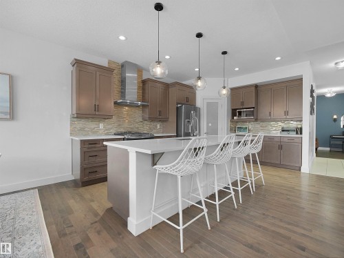 Kitchen featuring a breakfast bar, an island with sink, stainless steel appliances, hanging light fixtures, and tasteful backsplash - 3387 Parker Loop, Edmonton, AB - Indoor Photo Showing Kitchen With Upgraded Kitchen