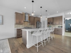 Kitchen featuring a breakfast bar, an island with sink, stainless steel appliances, hanging light fixtures, and tasteful backsplash - 