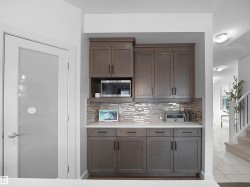 Kitchen with tasteful backsplash, dark wood finish cabinets, stainless steel microwave, light stone countertops, and light tile patterned flooring - 