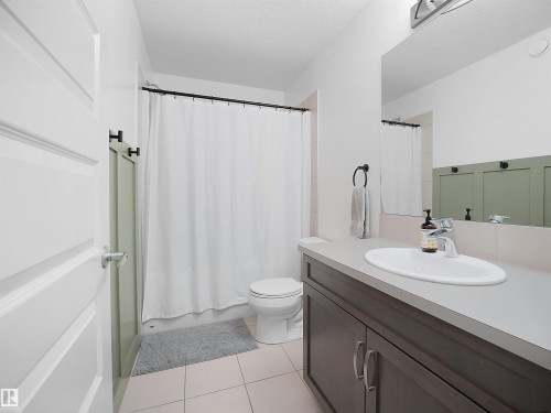 Full bathroom featuring vanity, a textured ceiling, light tile patterned floors, and shower / bathtub combination with curtain - 3387 Parker Loop, Edmonton, AB - Indoor Photo Showing Bathroom