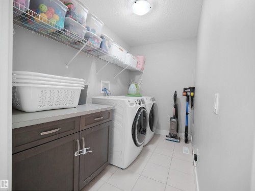 Laundry area with washer and dryer, a textured ceiling, cabinet space, and light tile patterned flooring - 3387 Parker Loop, Edmonton, AB - Indoor Photo Showing Laundry Room