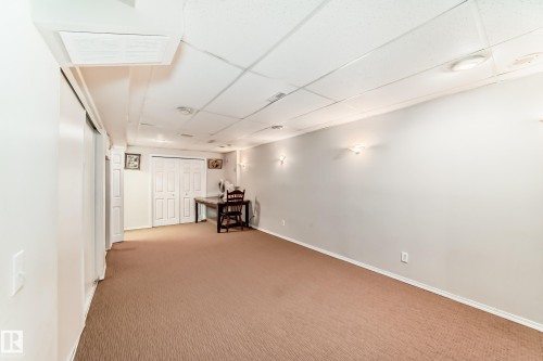The property features a spacious room with light brown carpet flooring and a suspended ceiling with recessed lighting - 11532 9 Avenue, Edmonton, AB - Indoor Photo Showing Other Room