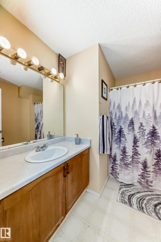 Bathroom featuring a vanity with a white countertop and a white sink, a mirror with a light fixture above it, and a shower with a patterned curtain - 11532 9 Avenue, Edmonton, AB - Indoor Photo Showing Bathroom