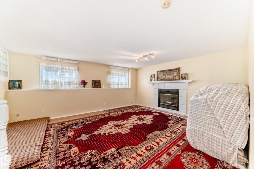 Living area featuring a fireplace with a white tiled surround, light-colored walls, and windows providing natural light - 11532 9 Avenue, Edmonton, AB - Indoor Photo Showing Living Room With Fireplace