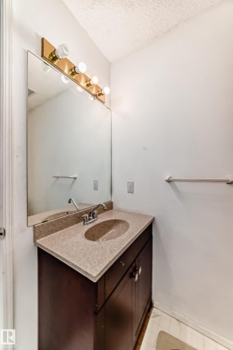 Vanity featuring a light-colored countertop with an integrated sink, a dark wood cabinet, and a large mirror with overhead lighting - 11532 9 Avenue, Edmonton, AB - Indoor Photo Showing Bathroom