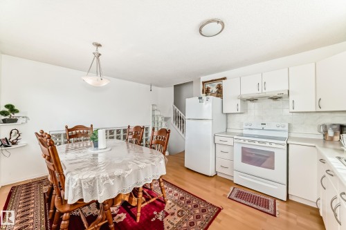The combined kitchen and dining area features white cabinetry, white kitchen appliances, and light hardwood flooring - 11532 9 Avenue, Edmonton, AB - Indoor Photo Showing Kitchen