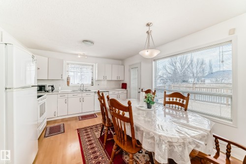This bright kitchen features white cabinetry, a large window above the sink, and a spacious dining area with hardwood flooring - 11532 9 Avenue, Edmonton, AB - Indoor Photo Showing Dining Room