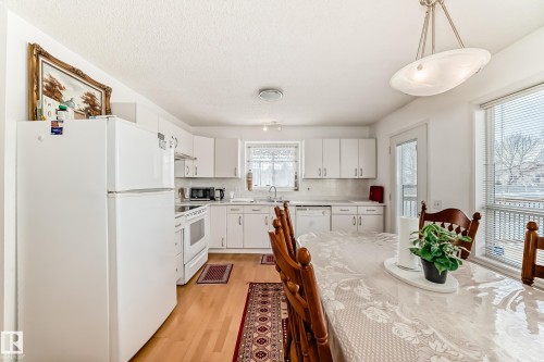 The kitchen features hardwood floors, white cabinetry, and white appliances - 11532 9 Avenue, Edmonton, AB - Indoor