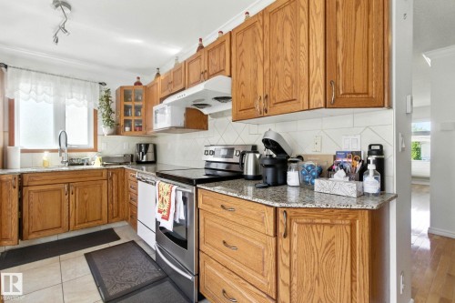 Kitchen with stainless steel electric range, wood finish cabinetry, backsplash, light stone countertops, and crown molding - 39 Grand Meadow Crescent, Edmonton, AB - Indoor Photo Showing Kitchen