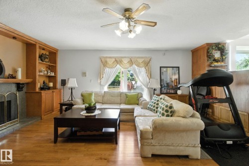 Living area featuring hardwood / wood-style floors, a ceiling fan, a textured ceiling, and a fireplace with raised hearth - 39 Grand Meadow Crescent, Edmonton, AB - Indoor Photo Showing Living Room With Fireplace
