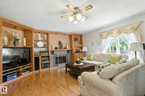 Living area with a ceiling fan, light wood-style floors, built in features, a textured ceiling, and a fireplace with raised hearth - 39 Grand Meadow Crescent, Edmonton, AB - Indoor Photo Showing Living Room With Fireplace